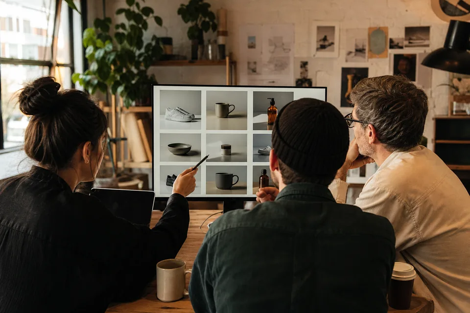 Three people in a review meeting seen from behind, looking at one monitor showing a grid of vertical product video frames
